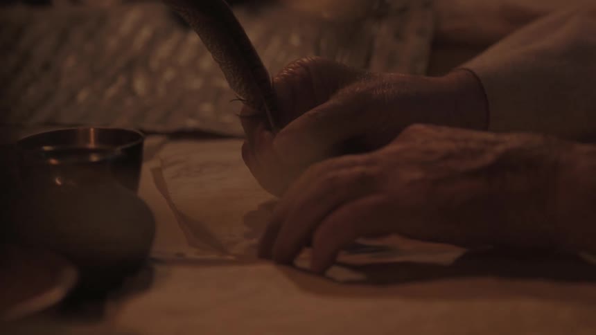An elderly person writes with a feather quill