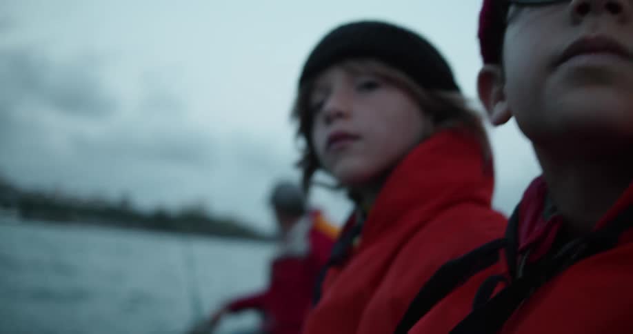 A pair of boys sit at the front of a boat as a man drives it from the rear on a cloudy day