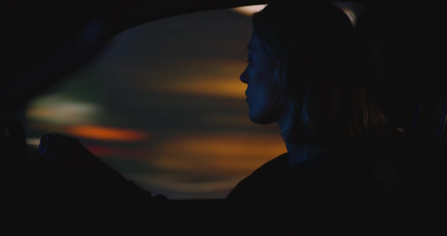 Side profile of blonde woman driving car in illuminated city street at night