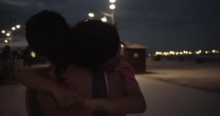 A mother carrying her son while walking outside on a sidewalk at night