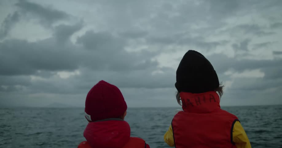 Boys wearing red coats and vests travel on boat floating on ocean water on a cloudy day