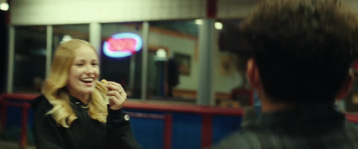 Girl wearing sweater and ripped jeans throws food pieces in boys mouth in front of restaurant