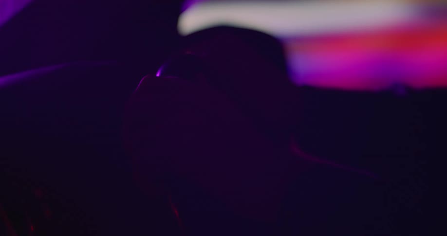 Close up of the hands of a person on the steering wheel of a car with colorful projections in the background