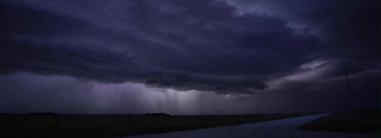 Dark storm front full of lighting rolls across road through countryside