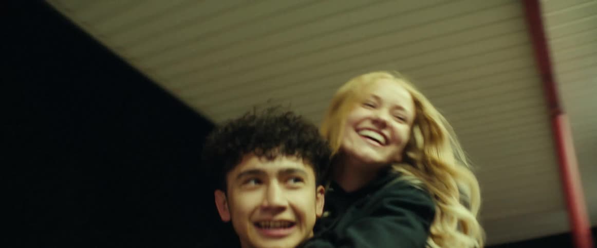 Boy carries blonde girl on his back laughing and running