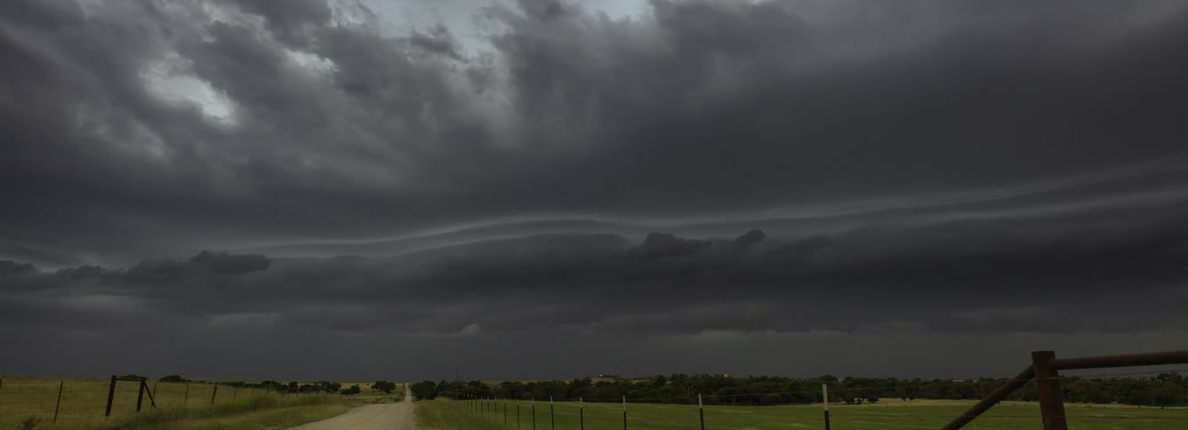 Dark storm clouds move across pastures as lightning strikes near road on the horizon