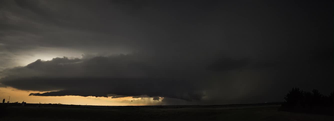 Lightning flashes in dark storm clouds as a tornado is in rotation and moving across the ground