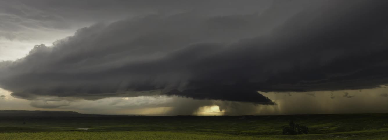 Dark storm clouds with pouring rain move over a rural area