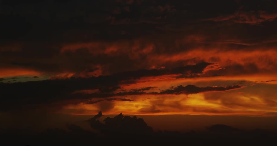 The sun appears red as it peeks through dark clouds over the coast