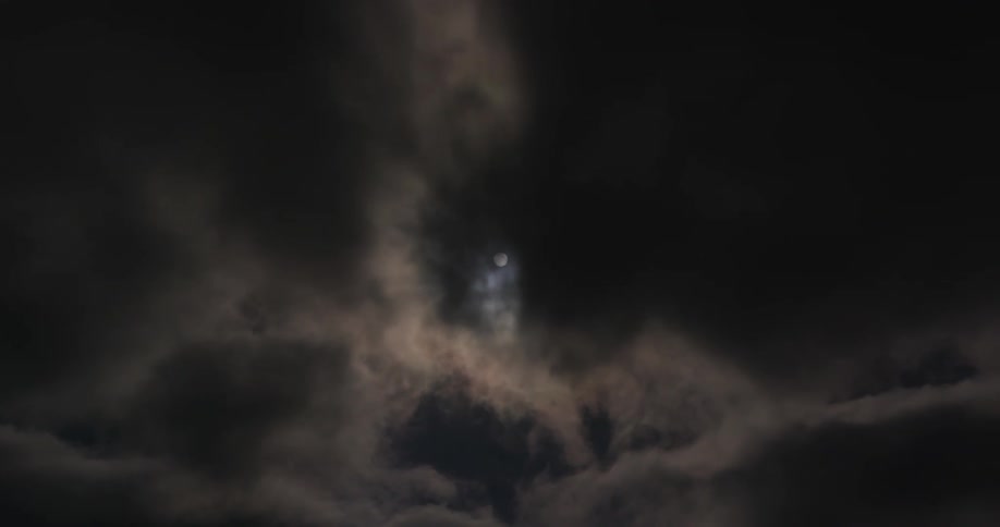 Full moon behind dark rolling clouds in the night sky