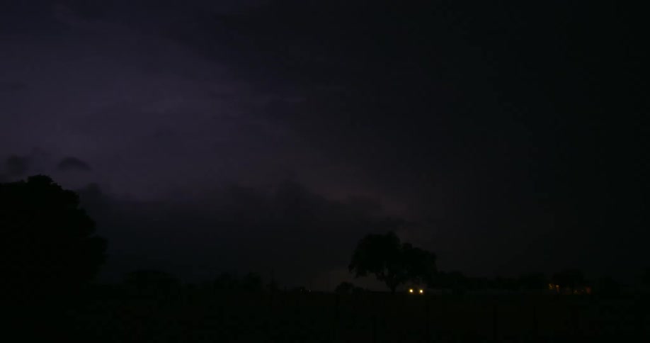 Lightning flashes in the clouds lighting the dark sky over a rural area