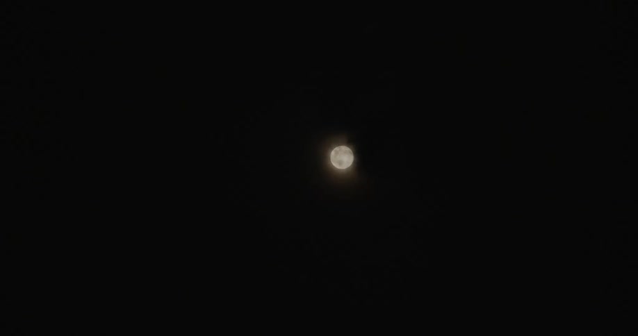 Full moon hides behind clouds in the night sky