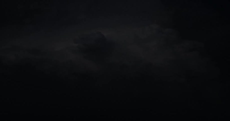 Lightning flashes brightly in the clouds illuminating the dark night sky