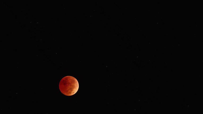 Red tinted moon moves through the dark of the night sky