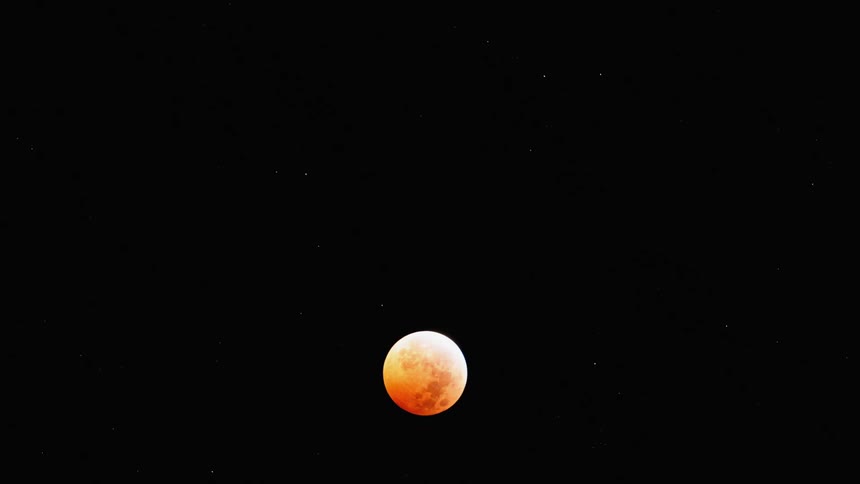 An orange moon moves south in the night sky