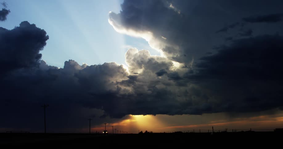 A lone truck travels on a long flat road with storm clouds covering most of the sky in the evening