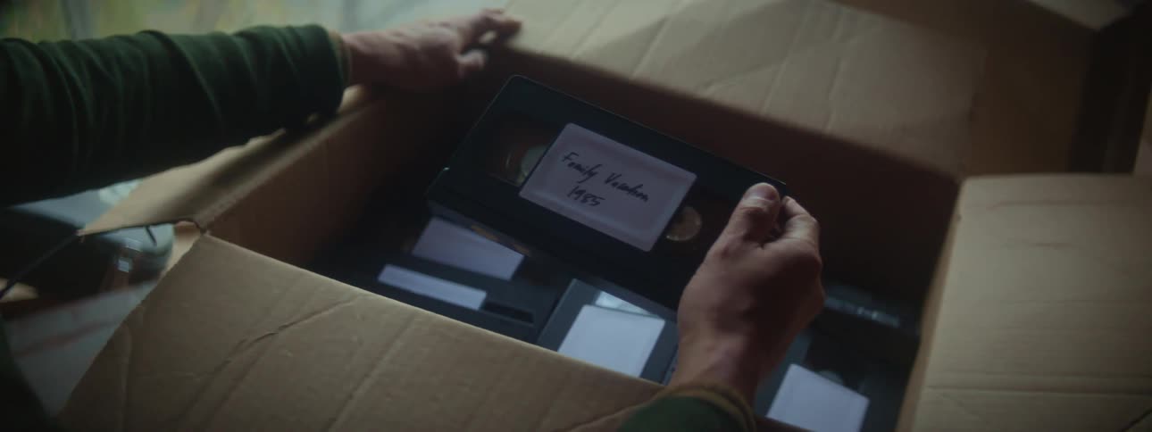 A man is looking through a box of vhs tapes with labels
