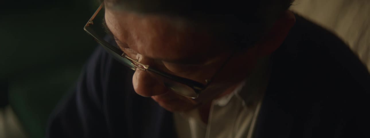 A man is sitting on a sofa in a home while looking down at something in the daytime