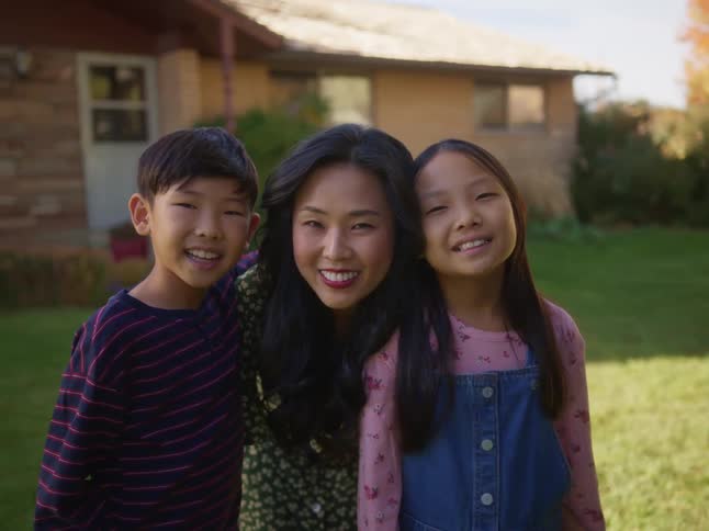 Happy asian mother taking a picture with her kids in front of a house