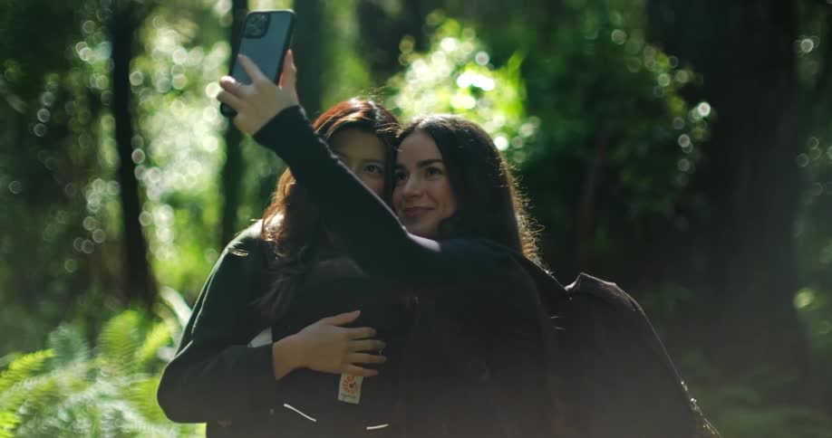 Two friends take selfies in front of the lush green vegetation of a forest