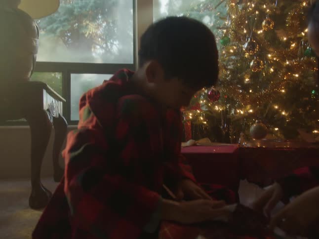 Mother smiles as her kids open christmas presents on floor near lit christmas tree