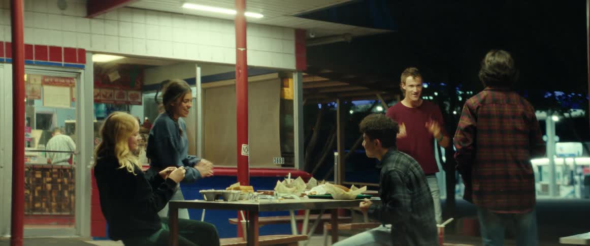 A group of teenage girls and boys sit at table eating food and joking with each other