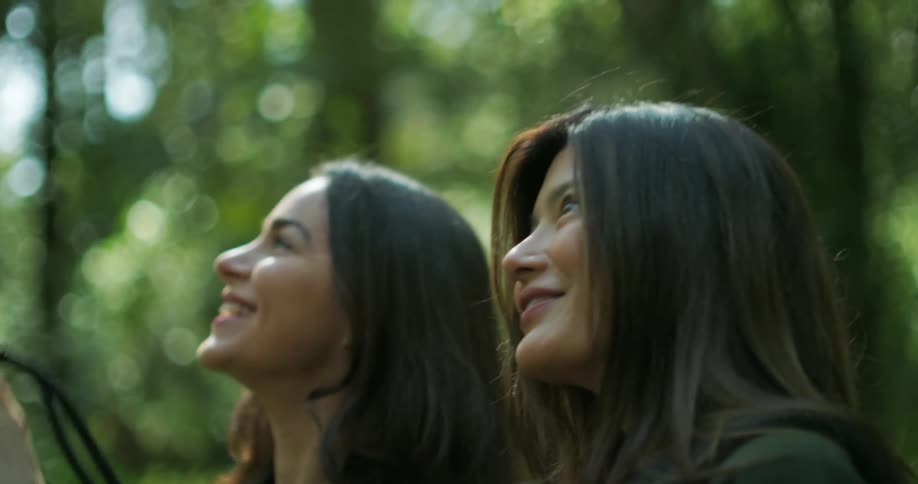 One woman pointing and holding a camera and smiling while another women smiles and looks in the same direction