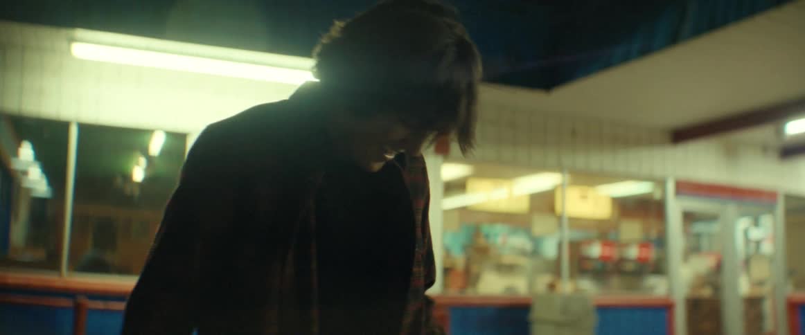 Teen boy practices skateboard trick in parking lot outside of diner at night