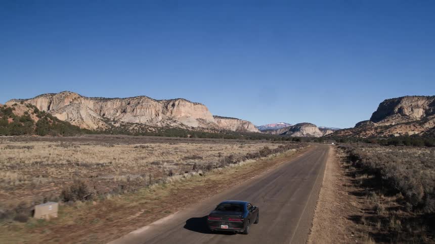 A black car drives down a road on a sunny day