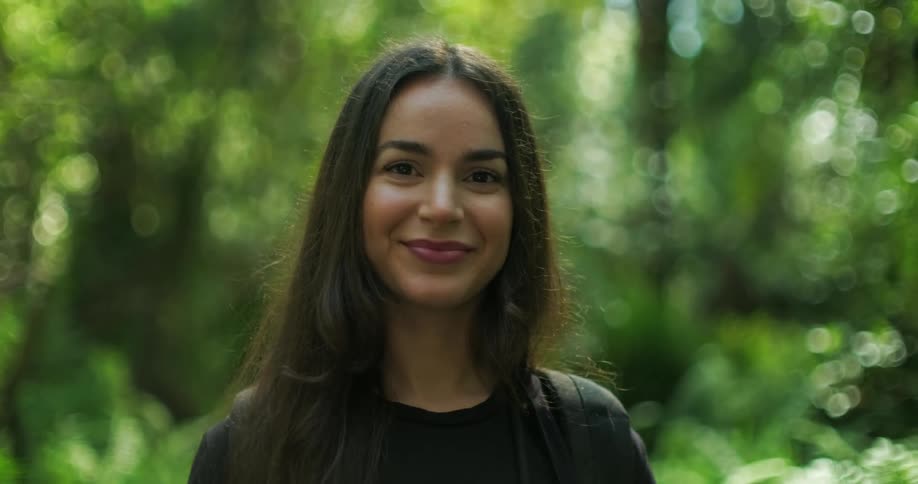 Close up of the face of a happy young woman standing in front of lush green vegetation