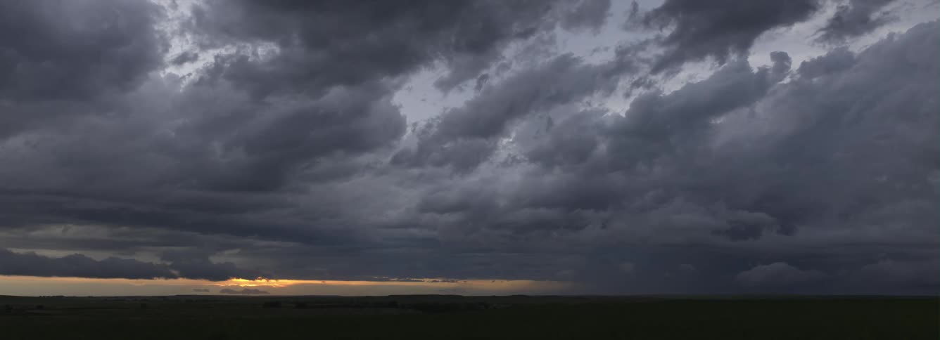 Darkening storm clouds cover the sky obscuring red horizon and sun
