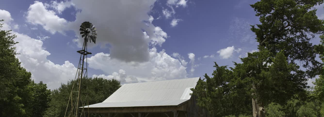 Clouds roll by a windmill near a white roof