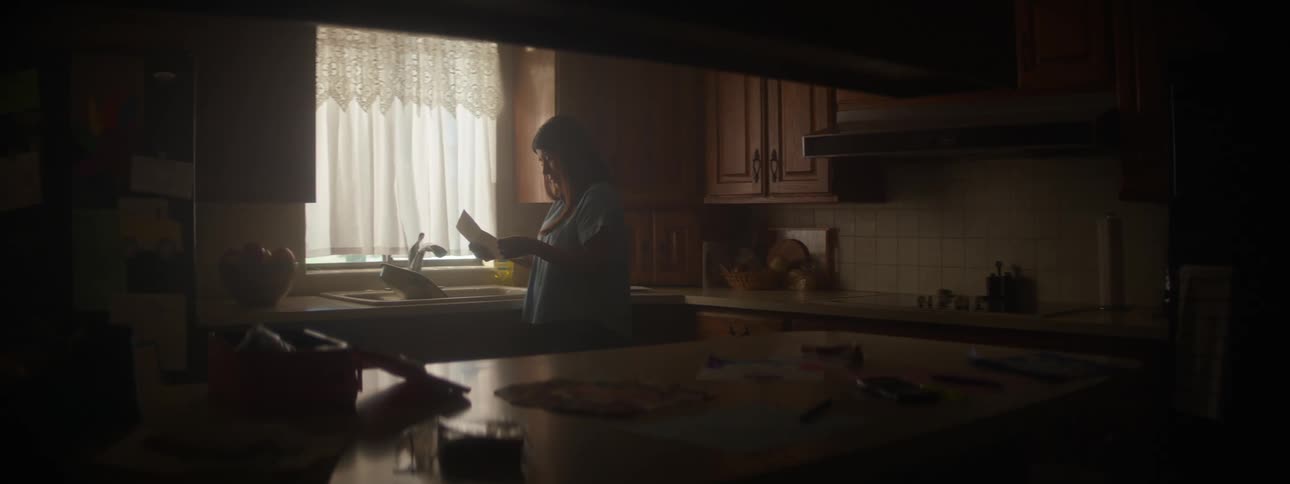 A woman is standing in her kitchen and reading a letter
