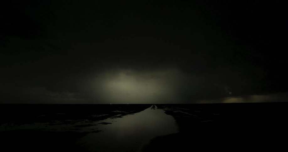 Lightning flashes in the clouds illuminating the dark night sky over a flooded field