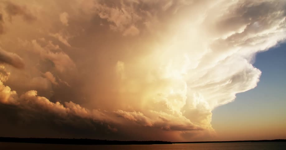 The sun shines brightly in the clouds as dark storm clouds move over the water