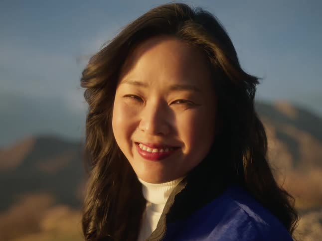An asian woman smiles at the camera with mountains in the background