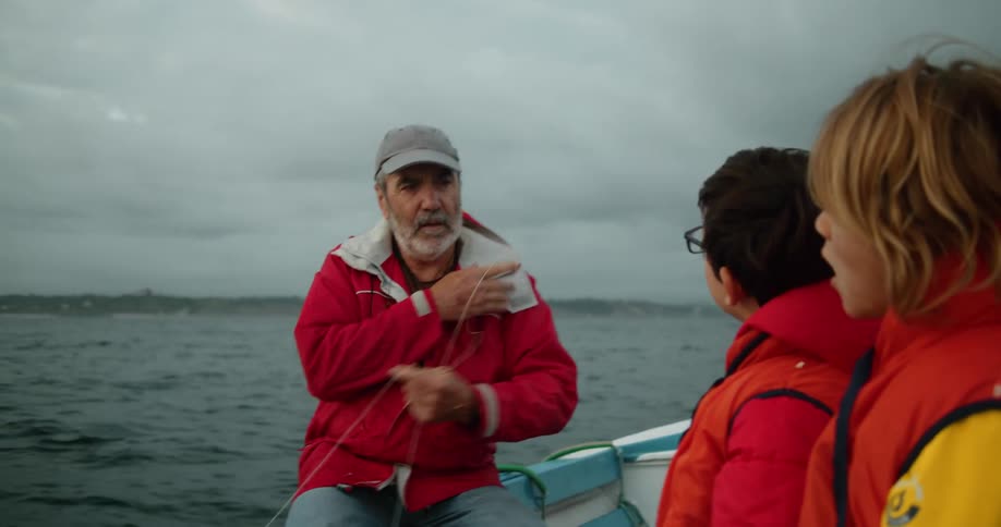 Kids sit in bobbing boat with grandfather watching him work with fishing line