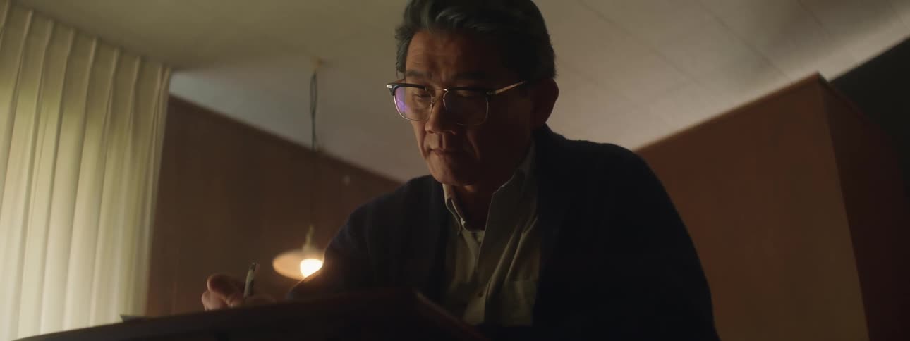A man writes while sitting at a desk indoors during the day
