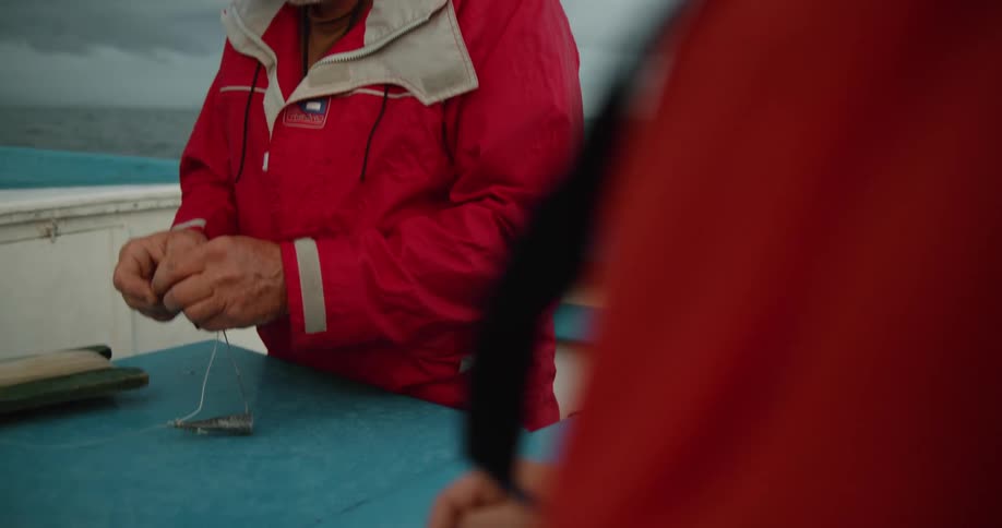 Man attaching a lure to a fishing line on a boat in the ocean