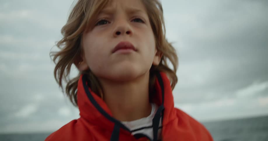 A little blonde boy wearing an orange coat looks up and down