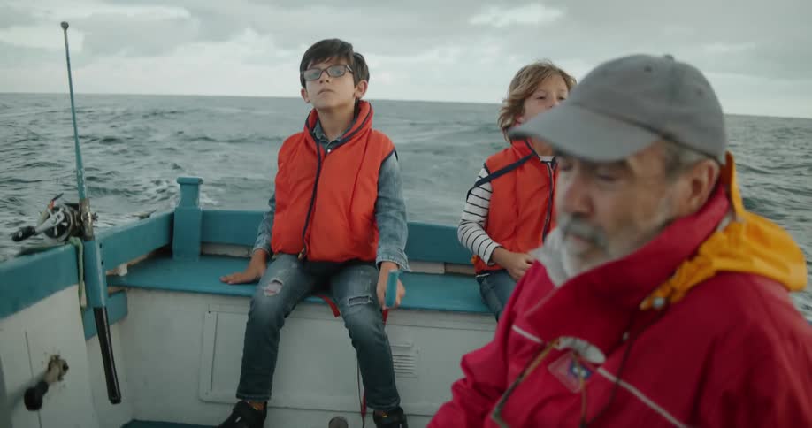 A man and a pair of boys travel on the ocean on a fishing boat on a cloudy day
