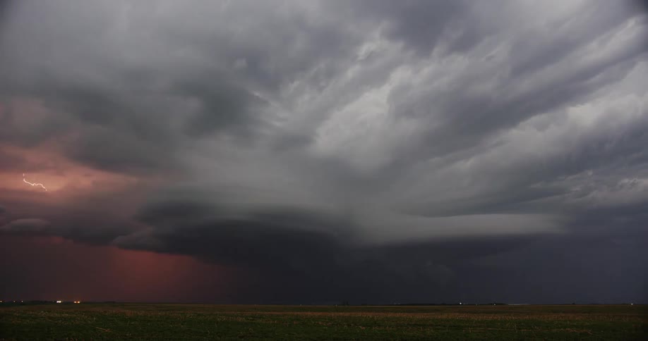 Thick clouds pass over a vast grassland during a thunderstorm at night