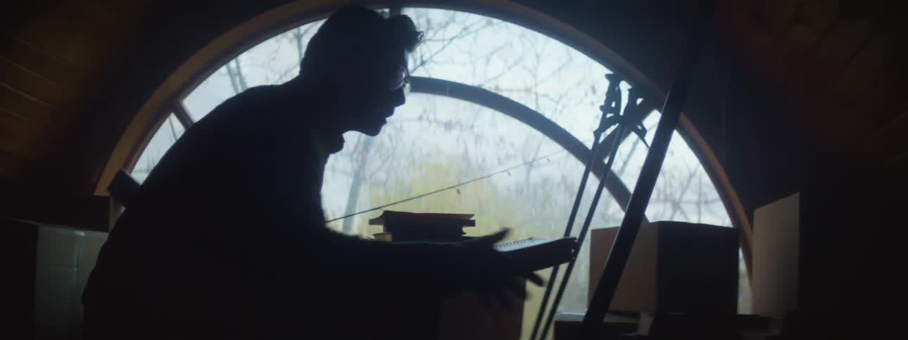 Silhouette of a man piling books over cardboard boxes on the attic