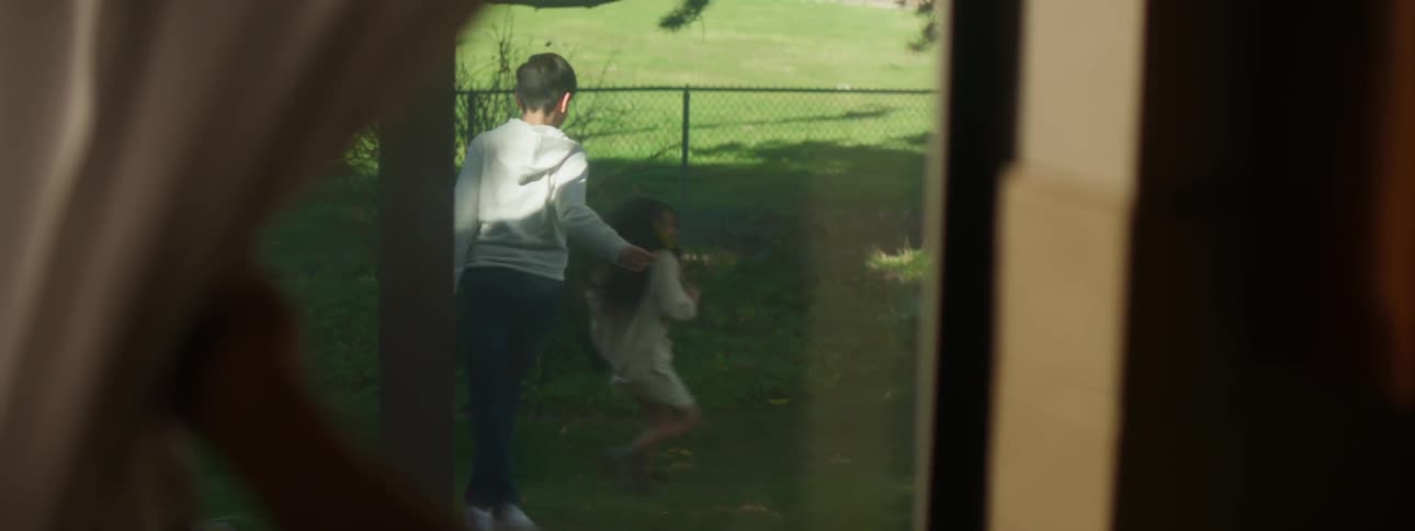 Mother opens a curtain to watch a her children playing in the backyard at home