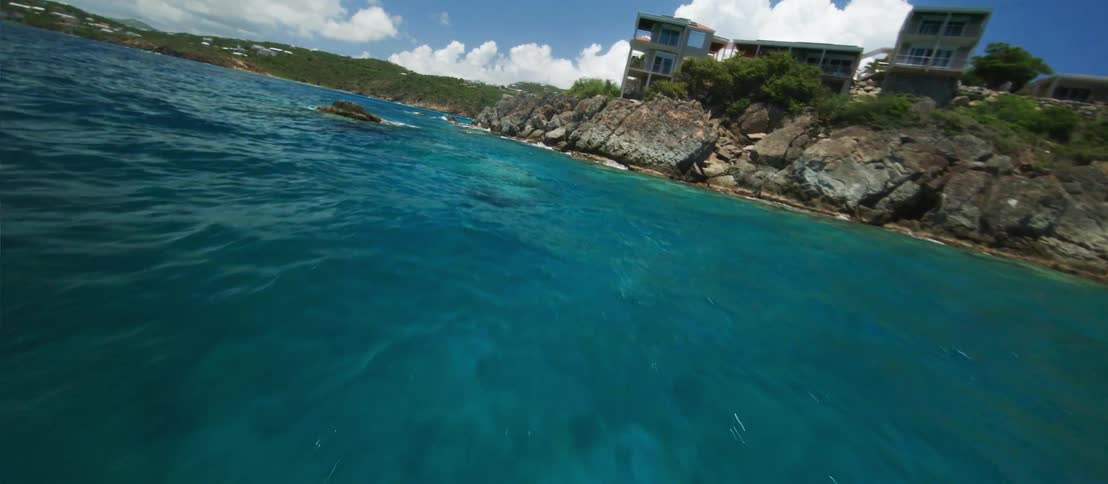 FPV - A point of view of someone moving through the water on some kind of vehicle is shown on a lake surrounded by rocks hills and a few homes