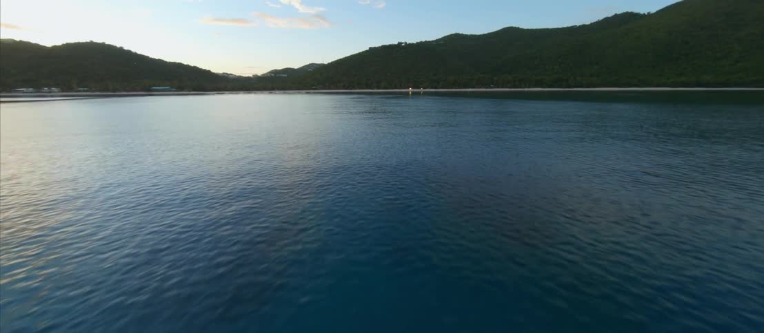 FPV - Aerial view of the calm surface of a lake close to the mountains at morning