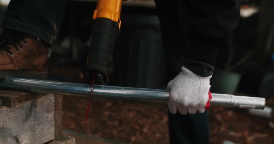 A farmer uses a saw to cut a pipe