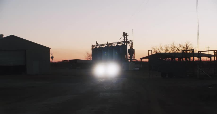 A pickup truck with headlights leaving the farm at sunset