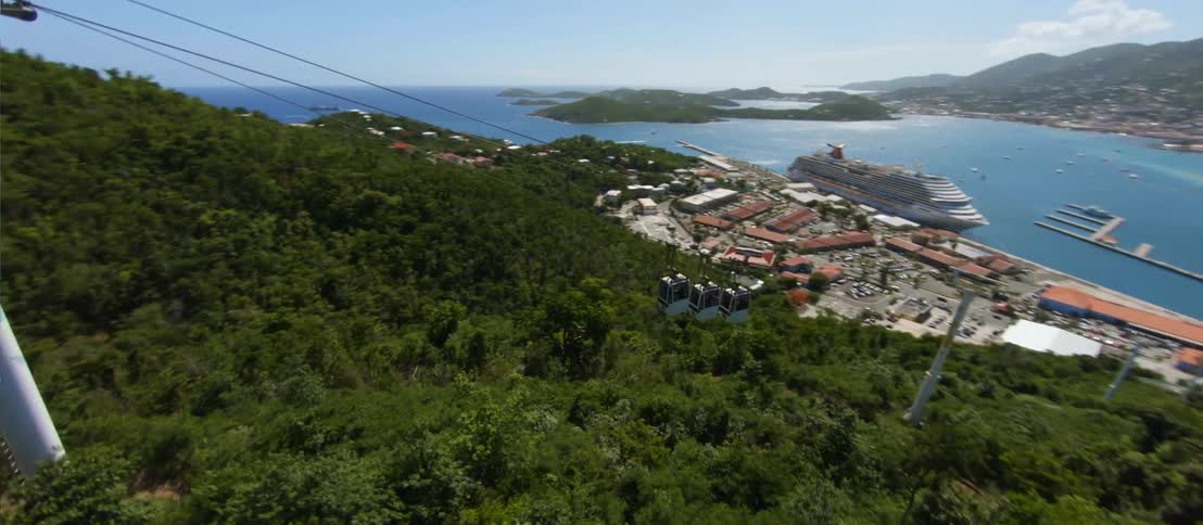 FPV - Aerial view of cable car and distant coastal city with cruise ship in the port