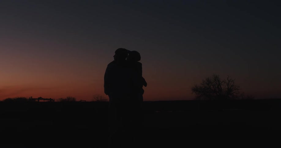 A couple hugs while looking across their land at sunset